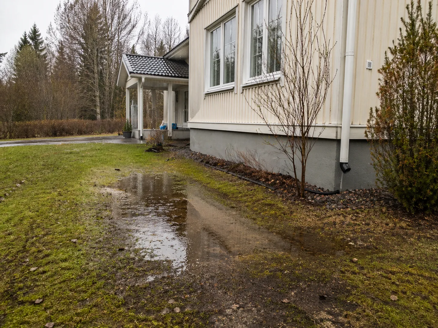 Seisovaa vettä talon pihassa, mikä viittaa kuivatusratkaisun tarpeeseen.